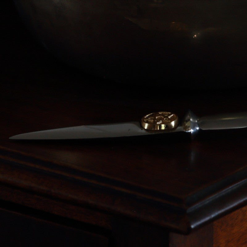 aluminium athame/ dagger with a gold pentacle beneath the hilt laying on a wooden table