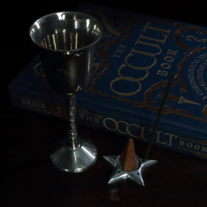 Aluminium Star Incense Holder with an incense stick and incense cone, in front of "The Occult Book" and silver chalice