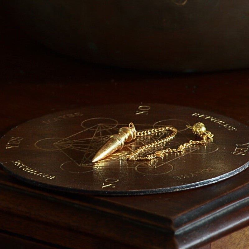 gold pendulum sitting on a wooden pendulum board