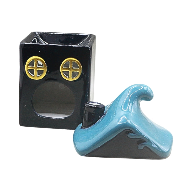 A small glossy ceramic figurine of a dark blue square house with two round gold window details, shown next to its light and dark blue wave-shaped lid on a plain white background.