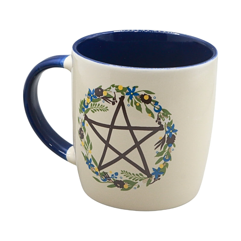 An off-white ceramic mug with a dark blue handle and interior, featuring a printed design of a black pentagram surrounded by a green and blue floral wreath.