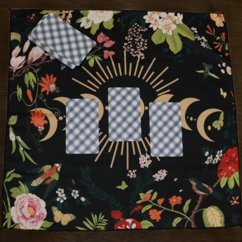 black tarot cloth with gold moon phases and floral design, with a 3 card spread and tarot deck on top