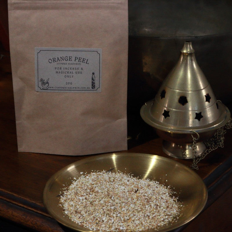 Bag of orange peel incense with a brass incense burner and dish of orange peel pieces on a wooden surface.