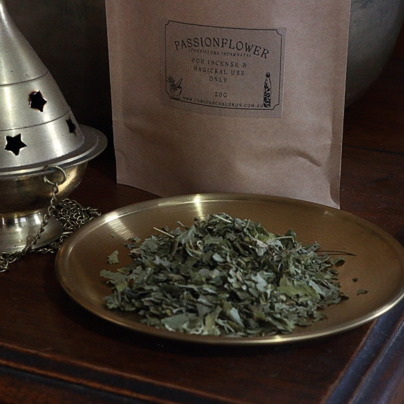 Dried herbs on a brass plate with a brown paper bag labeled 'Passionflower' in the background.