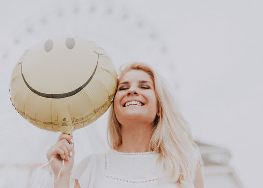 woman smiling holding a smily face foil balloon