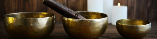 three singing bowls in a row on a wooden table with white candles in the background