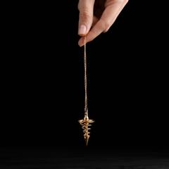 hand holding a gold spiral pendulum on a black background