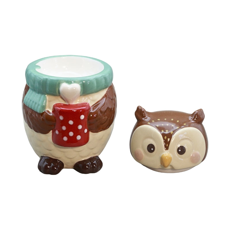 A ceramic holiday-themed set featuring an owl-shaped oil burner holding a red mug with white polka dots and a mint green scarf, alongside an owl-shaped container, on a plain white background.
