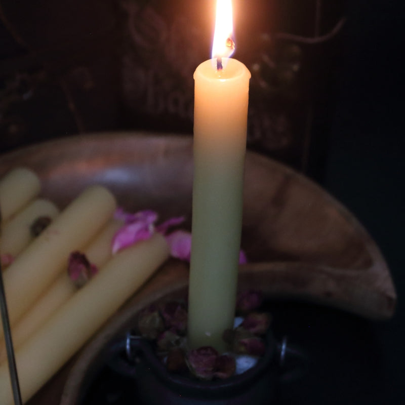lit beeswax candle sitting in a cauldron, in front of a wooden crescent moon shaped bowl 