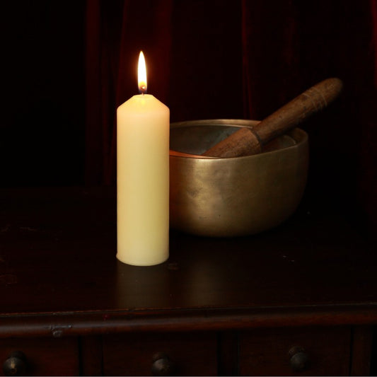 Beeswax pillar candle next to brass singing bowls