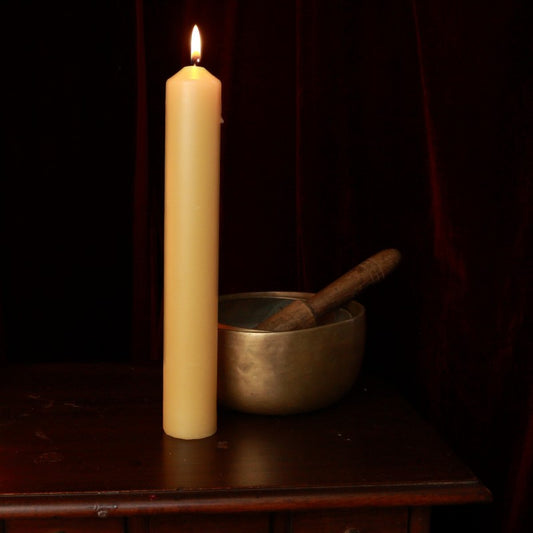 beeswax pillar candle 40mm x 250mm next to brass singing bowl