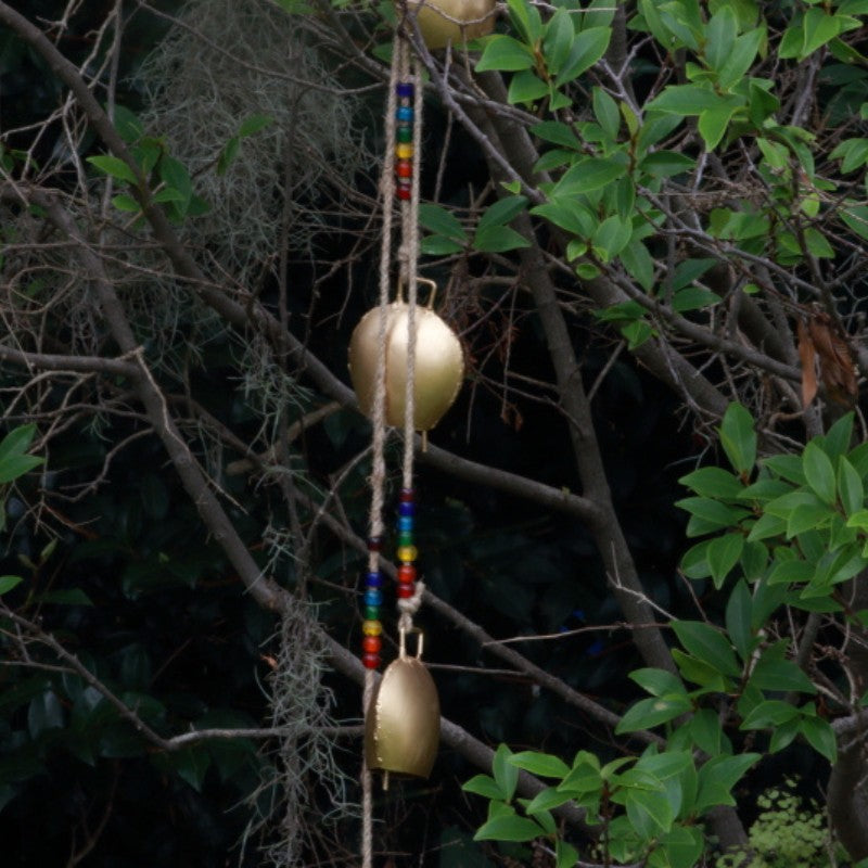 Cow Bells hanging from a beaded rope in front of a tree