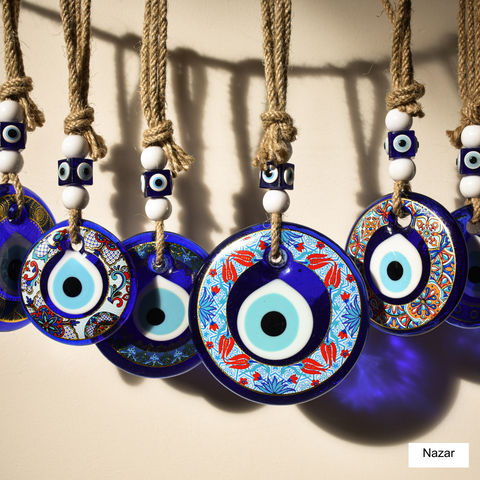 line of nazars- evil eye amulets (round bead shaped like an eye with concentric circles of dark blue, light blue, white and black)hanging from a string on a beige background