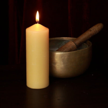 Beeswax pillar candle next to brass singing bowls