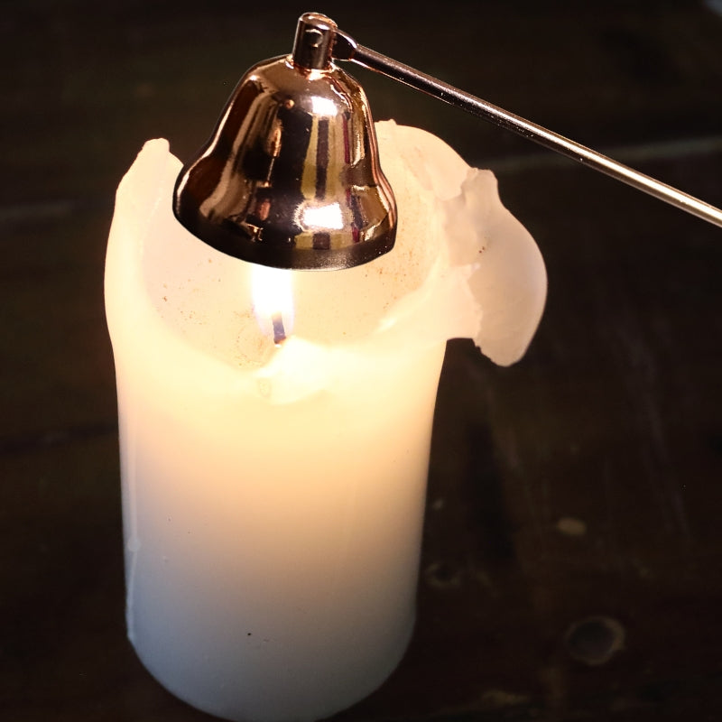 rose gold coloured candle snuffer perched over a lit white candle, on a wooden table