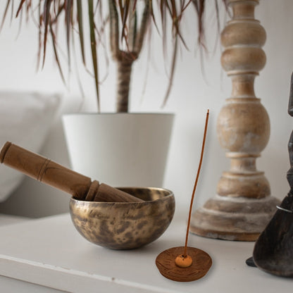 Round wooden carved incense holder- dark wood  on a table next to a singing bowl