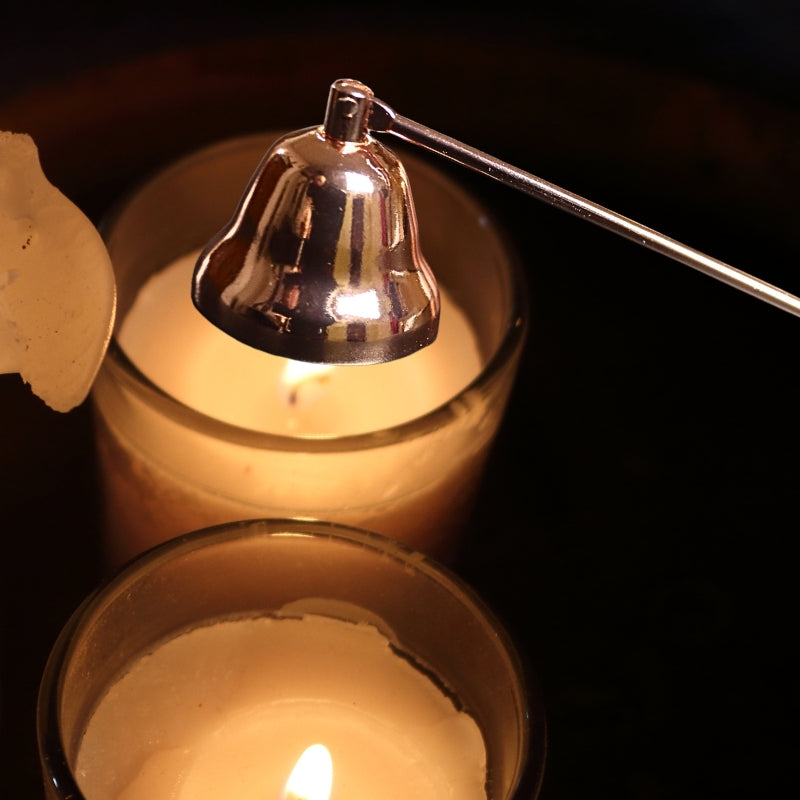 rose gold coloured candle snuffer, snuffing out 2 lit candles, one at a time, on a black background