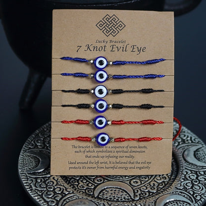 brown cardboard card with 6 corded bracelets, 2 red, 2 blue and 2 black, each with 7 knots and one nazar evil eye bead in the centre. Sitting on a silver embossed plate in front of a black cast iron cauldron with a pentacle on the front.