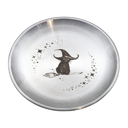 A round brushed silver metal bowl featuring a black illustration of a witch sitting on a broomstick, surrounded by stars and dots, on a white background.