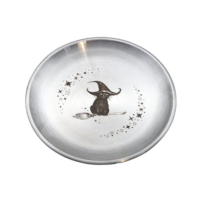 A round brushed silver metal bowl featuring a black illustration of a witch sitting on a broomstick, surrounded by small stars, on a plain white background.
