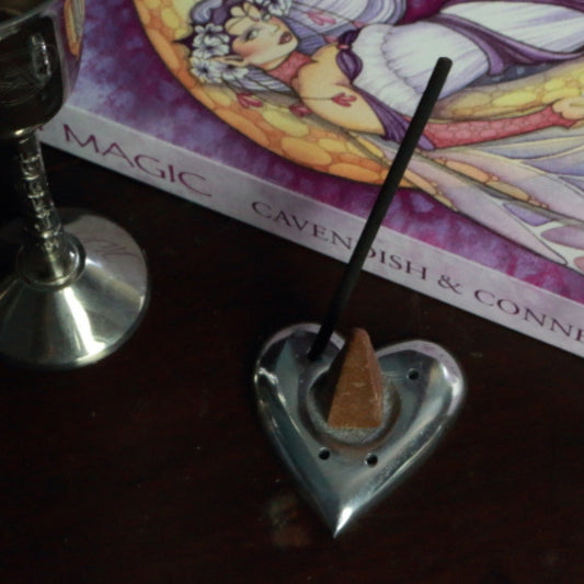 Aluminium Heart Incense Holder with an incense stick and incense cone, in front of a fairy book and silver chalice