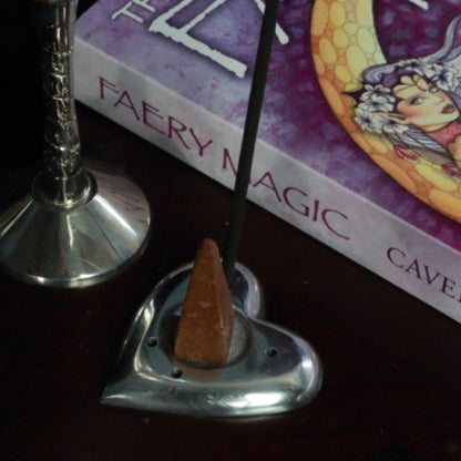Aluminium Heart Incense Holder with an incense stick and incense cone, in front of a fairy book and silver chalice