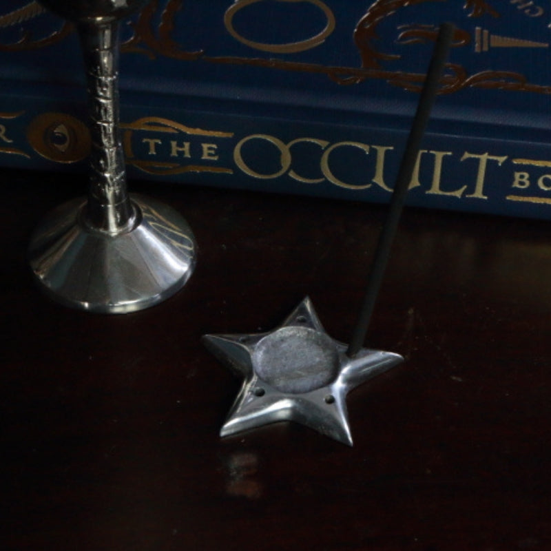 Aluminium Star Incense Holder with an incense stick, in front of "The Occult Book"  and silver chalice