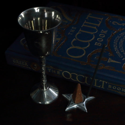 Aluminium Star Incense Holder with an incense stick and incense cone, in front of "The Occult Book"  and silver chalice