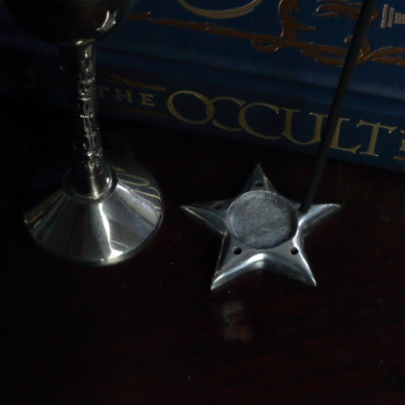 Aluminium Star Incense Holder with an incense stick in front of "The Occult Book"  and silver chalice