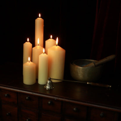 group of beeswax pillar candles on a wooden apothecary cabinet next to brass singing bowls and candle snuffer