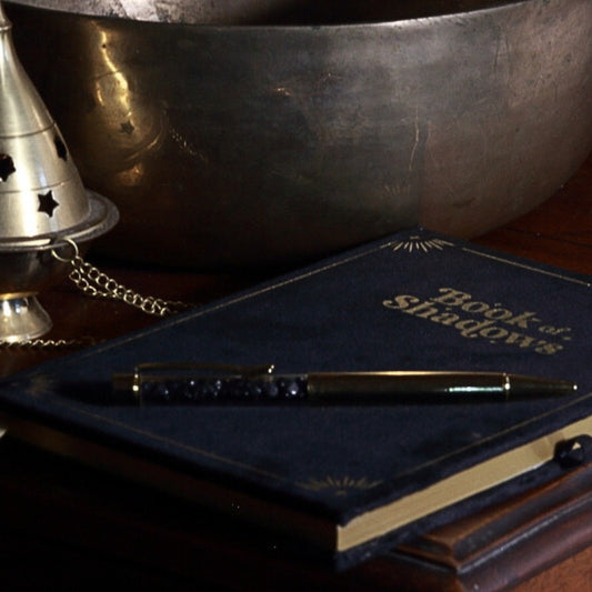 Velvet covered book of shadows in front of a brass bowl and censer with a black obsidian pen