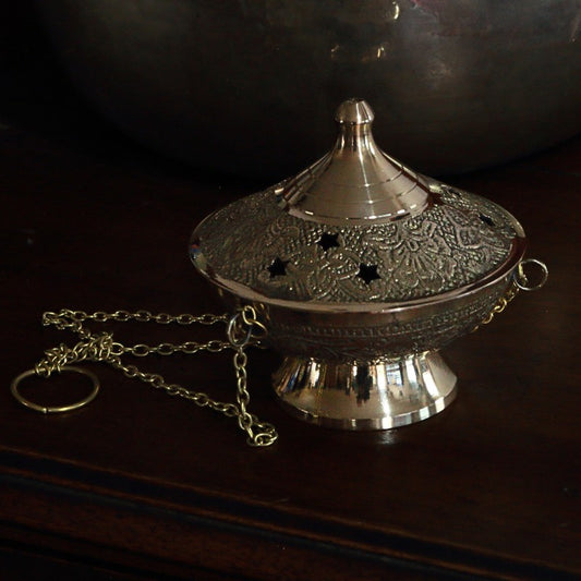Decorative brass incense holder with chain on a dark surface