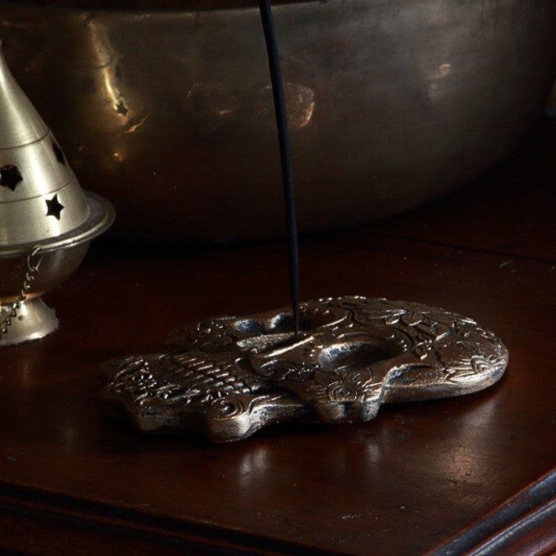 incense stick in a gold incense burner in a skull shape with floral designs on a wooden table