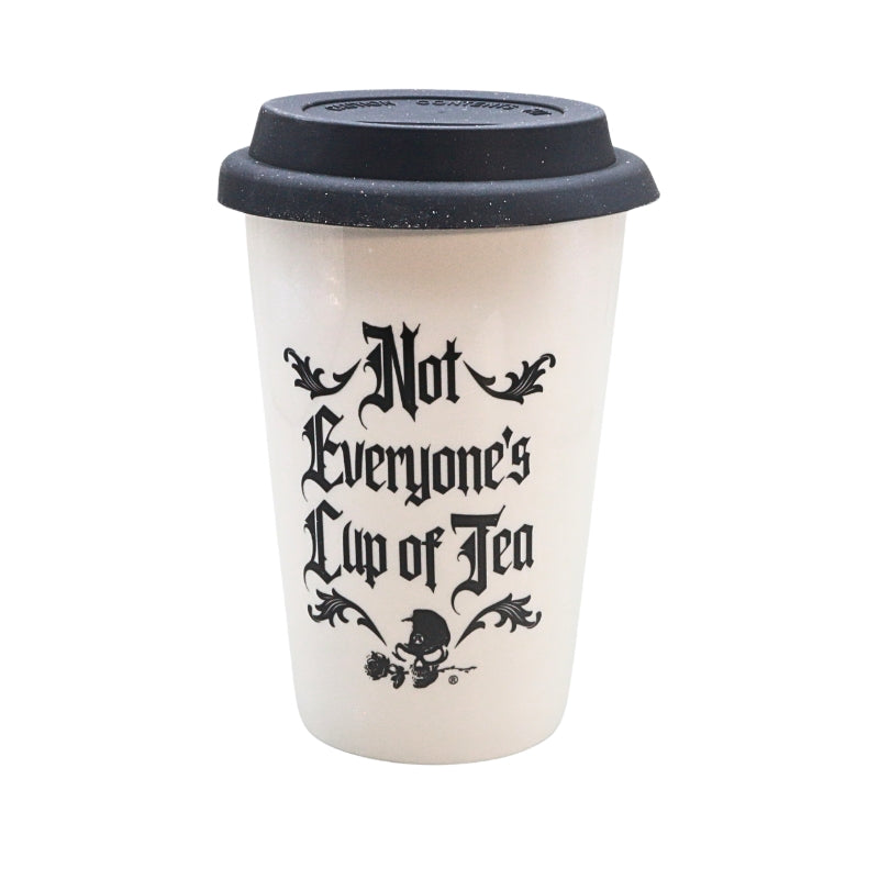 A reusable coffee cup with a black lid and a cream-colored body, featuring the text 'Not Everyone's Cup of Tea' in a black gothic font with decorative flourishes and a small skull-and-tea illustration at the bottom.