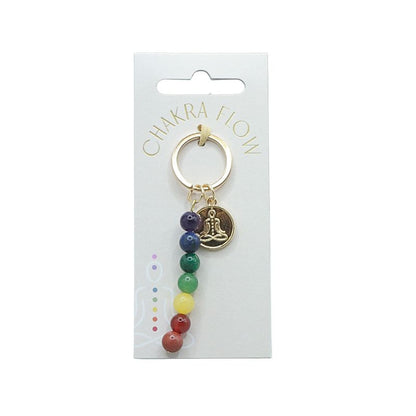 Gold keyring with rainbow coloured beads and a symbol of a person sitting in lotus pose on a white swing tag with the words "chakra flow"
