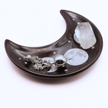 CRescent moon shaped ceramic trinket dish with a silver pendulum and quartz crystal point