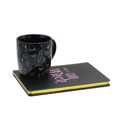 Black mug with decorative patterns on a black journal with 'today im a  good Witch' text, on a white background