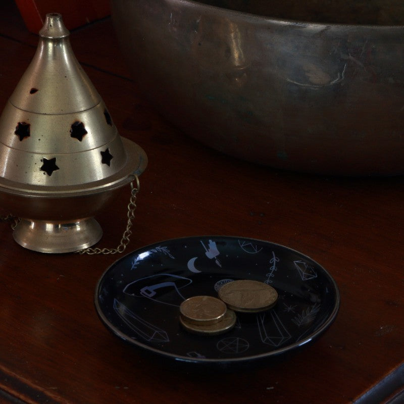 brass incense burner on a wooden surface with coins on a black plate.