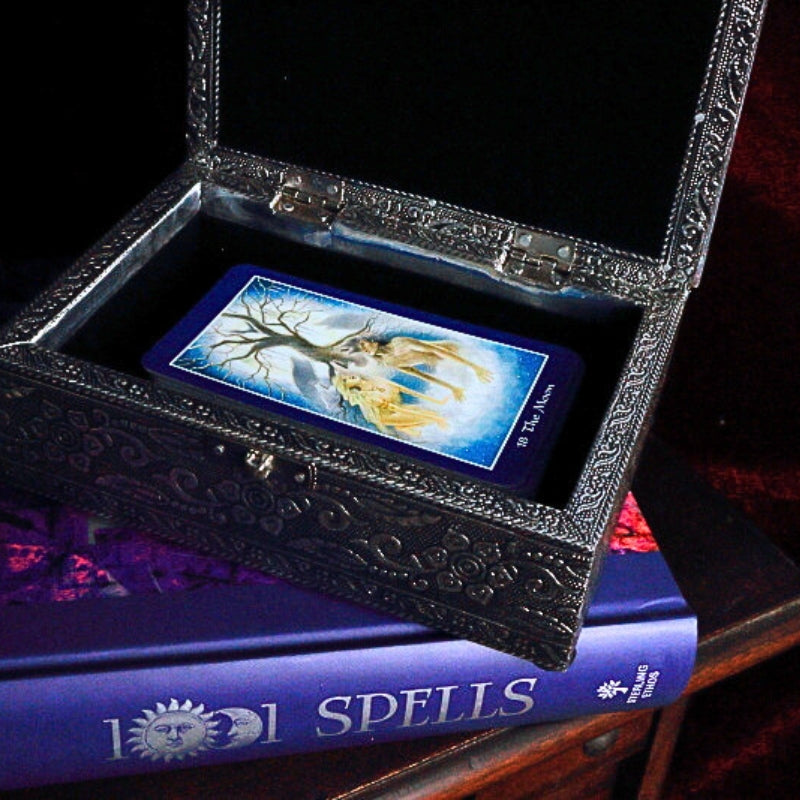 Embossed Metal Tarot Box open with shapeshifter tarot cards inside,  on top of a book of spells