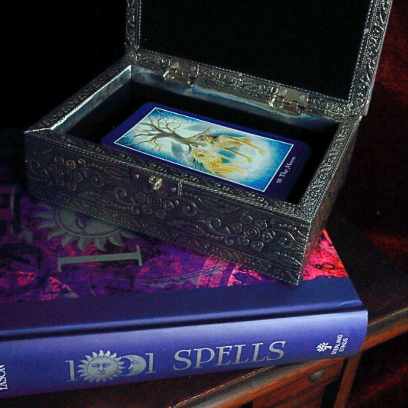 Embossed Metal Tarot Box open with shapeshifter tarot cards inside,  on top of a book of spells