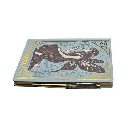 blue and gold notebook with a grey vintage style fairy on the cover, and a gold pen at the side, on a white background