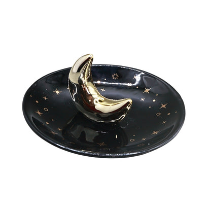 A glossy black ceramic dish decorated with small gold stars and a raised metallic gold crescent moon topper, shown on a plain white background.