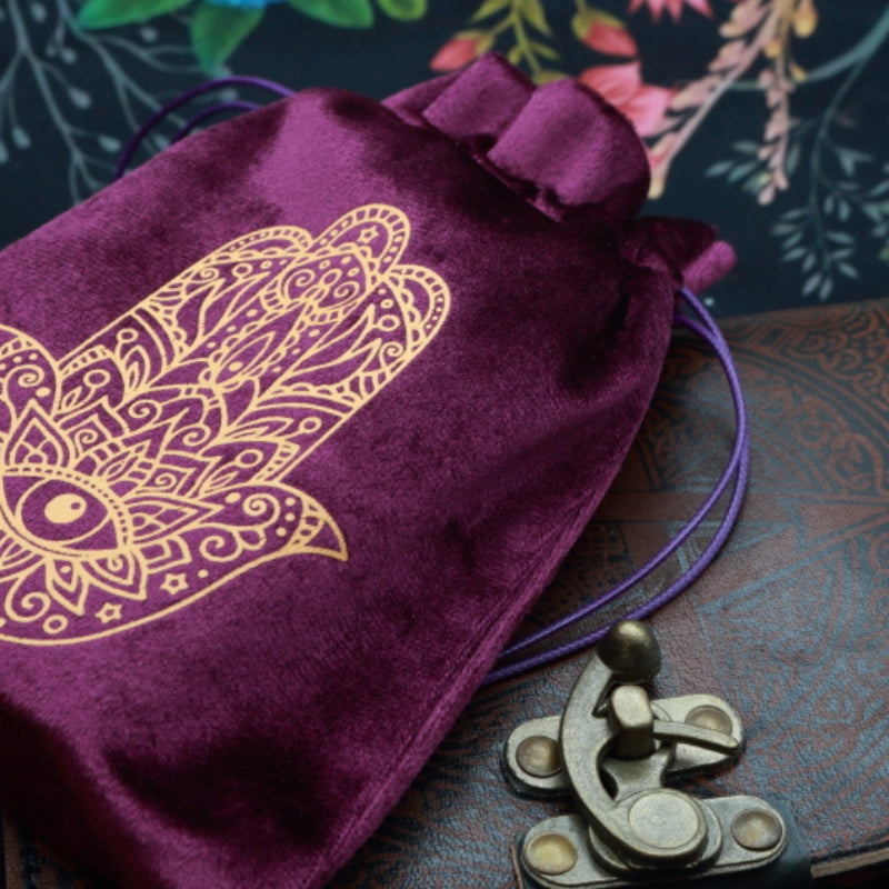 purple and gold Hamsa Hand Tarot Bag for Tarot and Oracle Cards laying on a brown leather journal