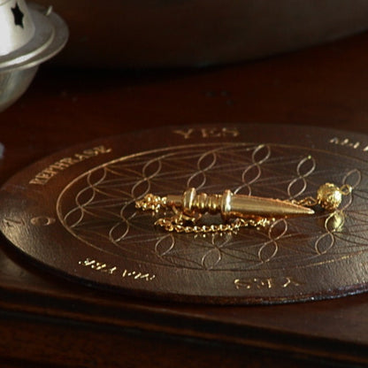  gold pendulum sitting on a flower of life design on wooden pendulum board