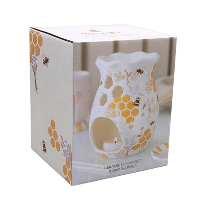 A ceramic oil burner and wax warmer with a white body, decorated with yellow honeycomb patterns, small flowers, and bumblebees, shown in its retail packaging box.