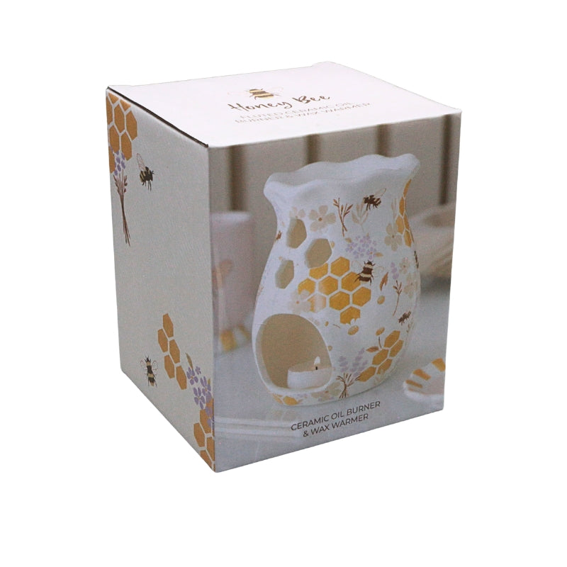A white ceramic oil burner and wax warmer with yellow honeycomb and floral patterns, shown inside its white retail box with printed bee and honeybee illustrations.