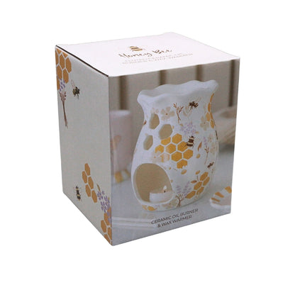 A white ceramic oil burner and wax warmer with yellow honeycomb and floral patterns, shown inside its white retail box with printed bee and honeybee illustrations.