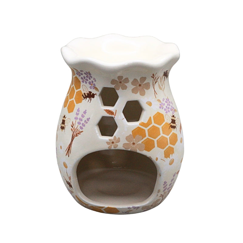 A ceramic oil burner candle holder with a white base decorated with orange honeycomb patterns, purple lavender sprigs, brown flowers, and small bumblebees. It features a scalloped rim, hexagonal cutouts, and a lower arched opening.