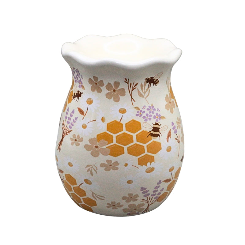 A ceramic wax warmer with a scalloped rim, decorated with a pattern of orange honeycombs, purple flowers, and brown bees on a cream-colored background.