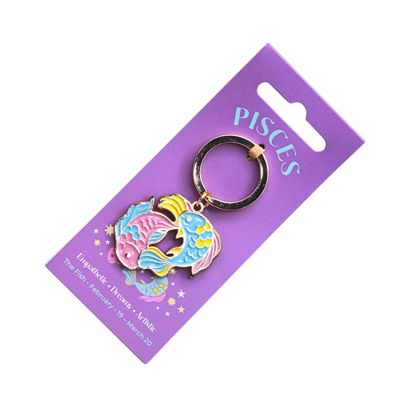 An enamel Pisces zodiac keychain featuring two fish in pink, blue, and yellow, attached to a purple cardboard display card with 'PISCES' printed in light blue.